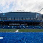 Business professionals discussing Cardiff Rugby takeover negotiations in a modern office.