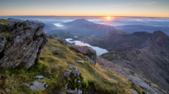 Visitors in professional attire enjoying the sunrise at Eryri National Park, highlighting parking concerns.