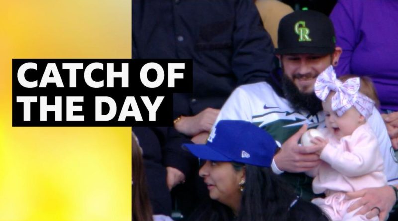 A father catches a baseball with baby in hand at a baseball game.