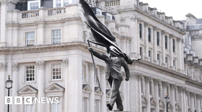 A crowd admires a Banksy-style sculpture in a London park.