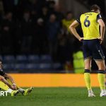 Oxford United relegation scene with players in professional attire discussing strategies.
