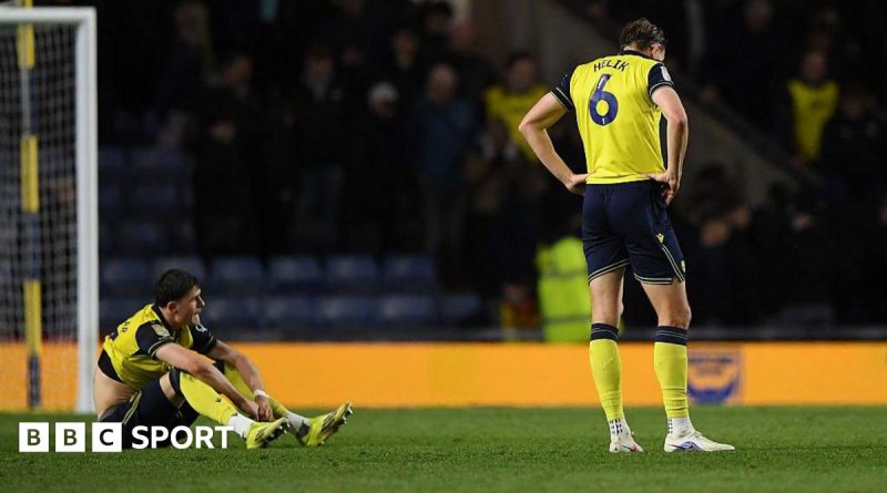 Oxford United relegation scene with players in professional attire discussing strategies.