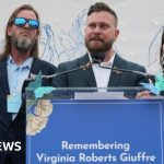 Virginia Giuffre vigil with attendees holding candles and signs in remembrance.