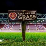 Excited football fans watching a Scottish Premiership match in the stadium.