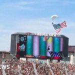 Skydiver incident at football game with responders and jumbotron.