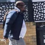 Police discussing the Golders Green stabbing suspect case in a busy urban area.