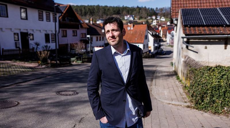 Syrian refugee mayor leading a community discussion in formal attire.