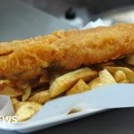 Chefs preparing traditional fish and chips in a busy kitchen setting.